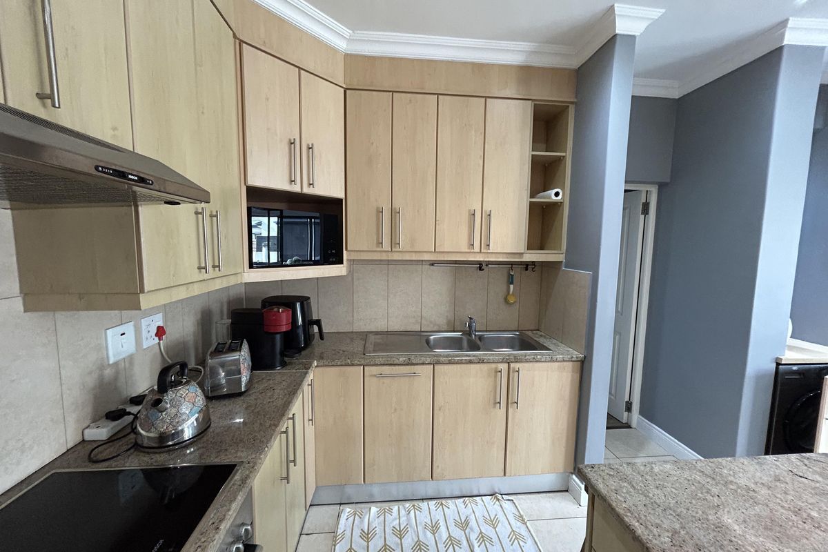 A functional kitchen featuring light wood cabinetry, granite countertops, a stainless steel sink, and a built-in extractor fan.