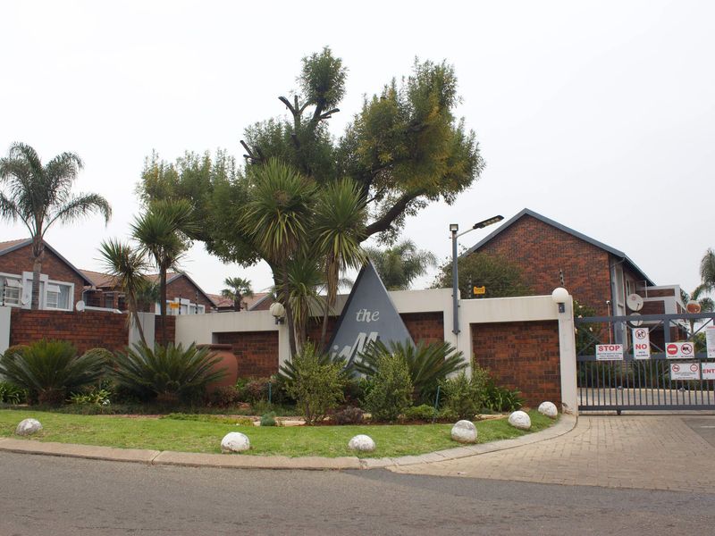 Front entrance view of the apartment complex featuring a brick boundary wall, security gate, and landscaped garden area.