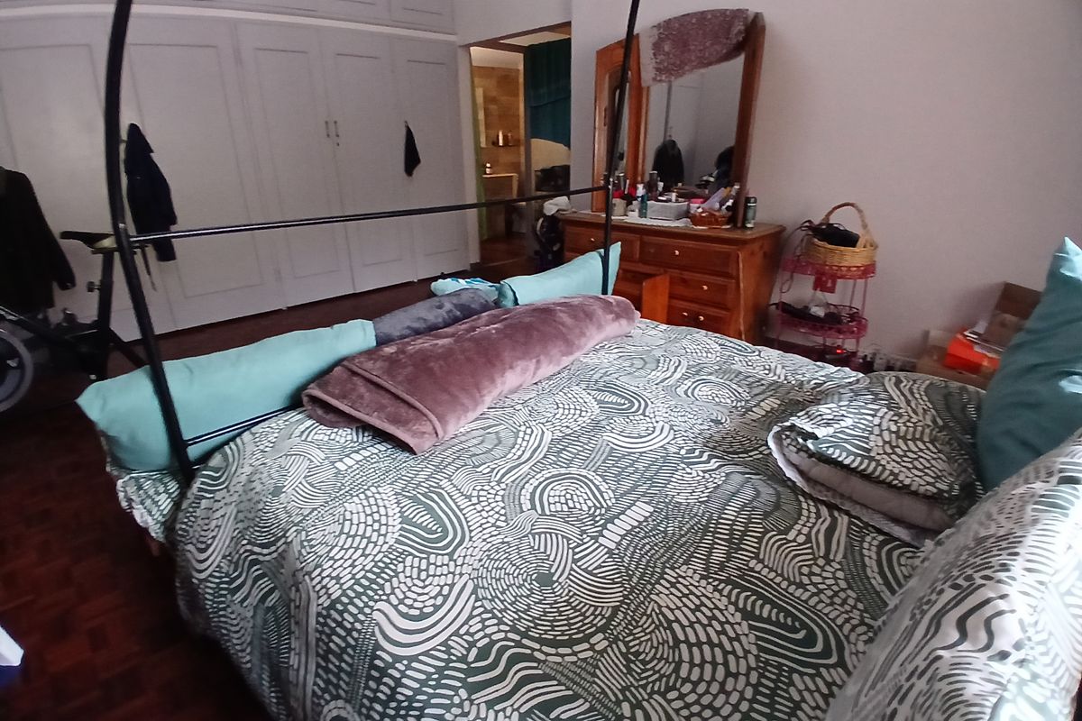 A bedroom featuring built-in cupboards and parquet flooring, with an adjoining view into a bathroom area.