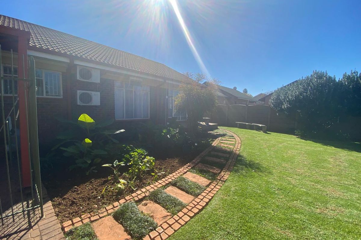 A well-maintained rear garden featuring a curved brick pathway, manicured lawn, and established landscaping adjacent to the brick house exterior.