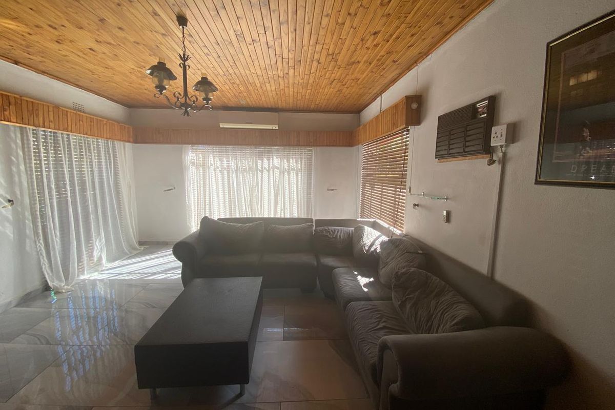 Spacious living room featuring polished floor tiles, a timber-clad ceiling, and wall-mounted air conditioning unit, offering a functional and well-lit living space.