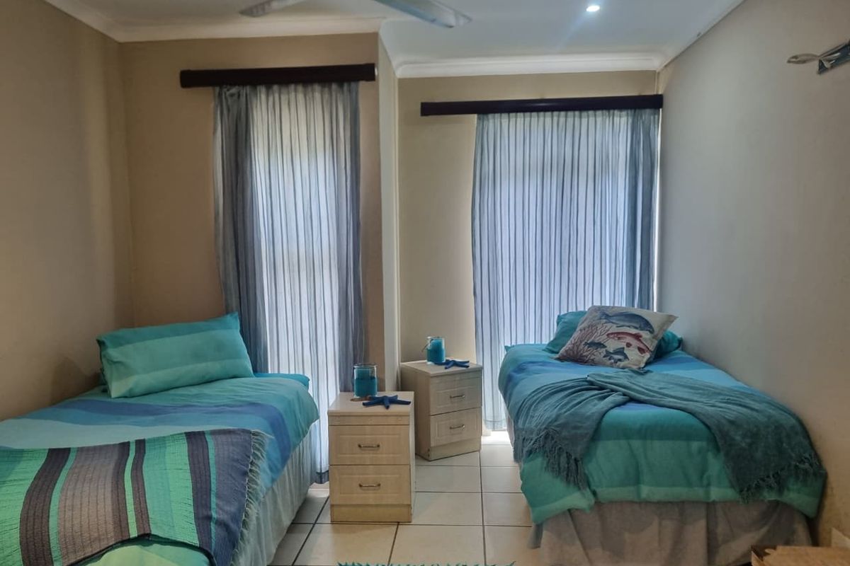 A bedroom featuring tiled flooring, a ceiling fan, and two large windows with curtain tracks, providing natural light and ventilation.
