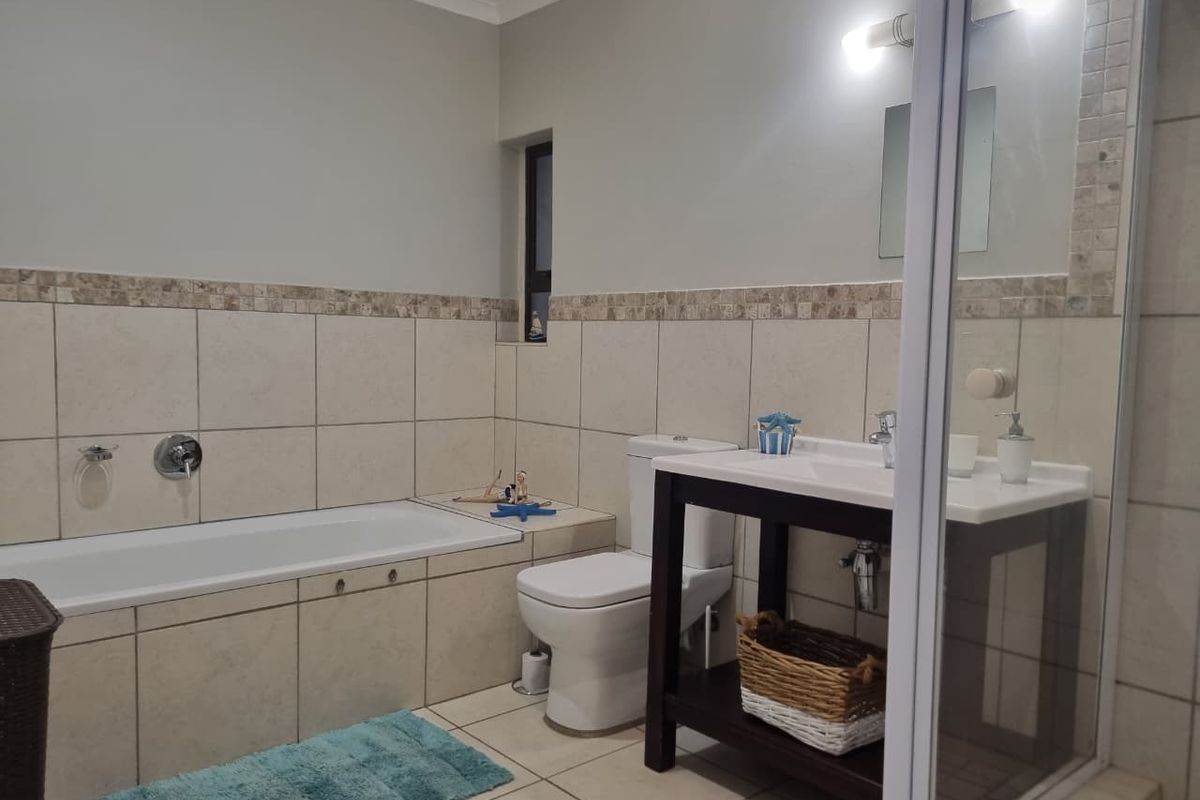 A well-maintained bathroom featuring a built-in bathtub, a separate shower enclosure, a modern vanity unit, and neutral wall and floor tiling.