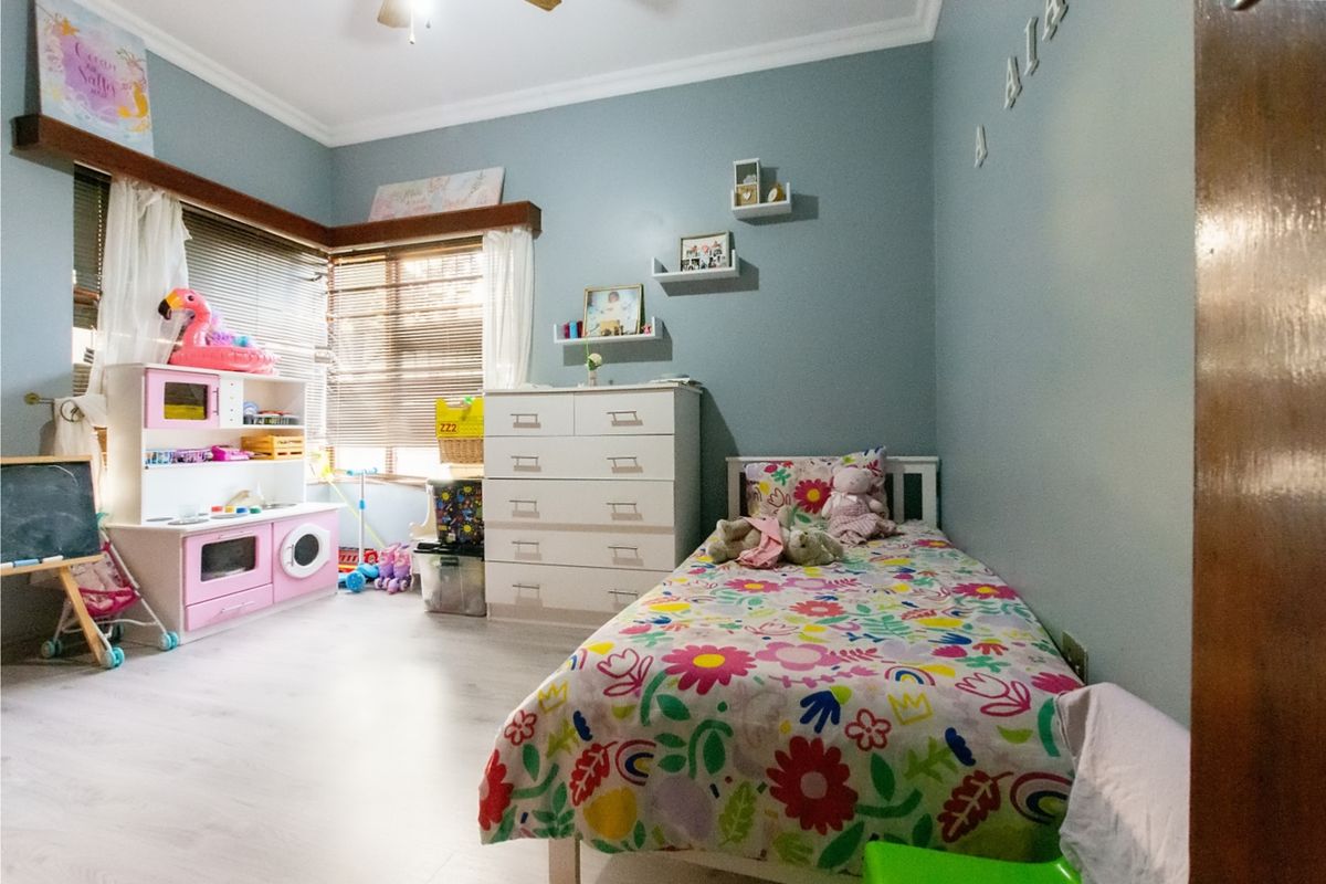 A bedroom featuring light-toned laminate flooring, crown molding, and large windows with fitted blinds, providing a bright and functional living space.
