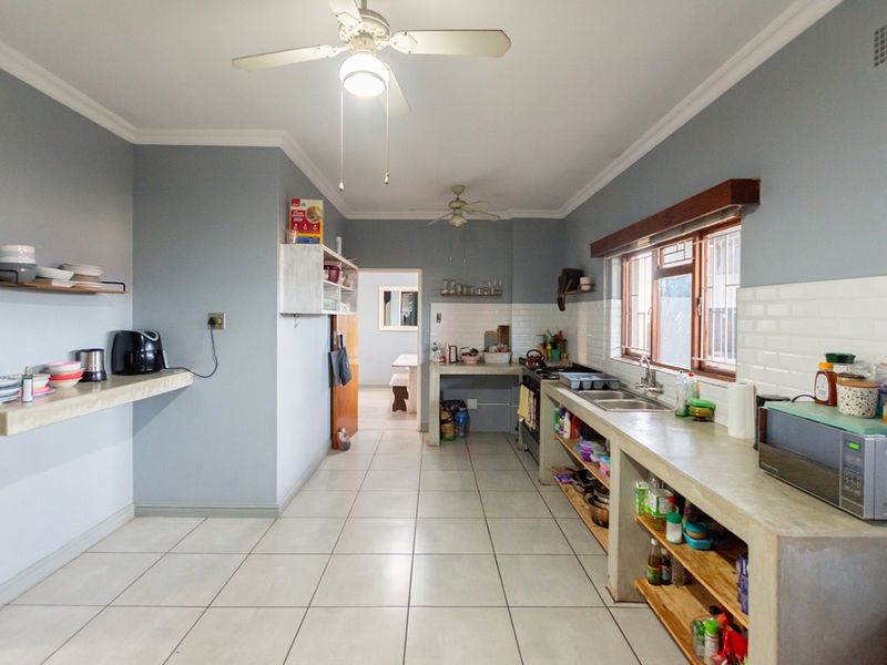 A functional kitchen featuring concrete countertops, open shelving, tiled flooring, and a double sink, with a view through to an adjacent dining area.