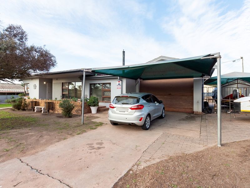 Front exterior view of the house featuring a paved driveway, a large shade-cloth carport, and a brick-walled entrance patio.