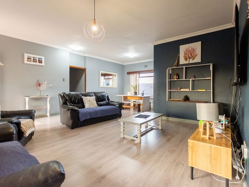 Spacious open-plan living area featuring light wood-look laminate flooring, modern pendant lighting, and a bold dark blue accent wall.