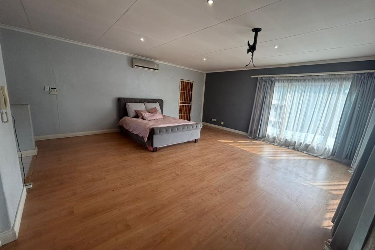 Spacious bedroom featuring laminate flooring, recessed ceiling lighting, a wall-mounted air conditioning unit, and a large window with curtain tracks.