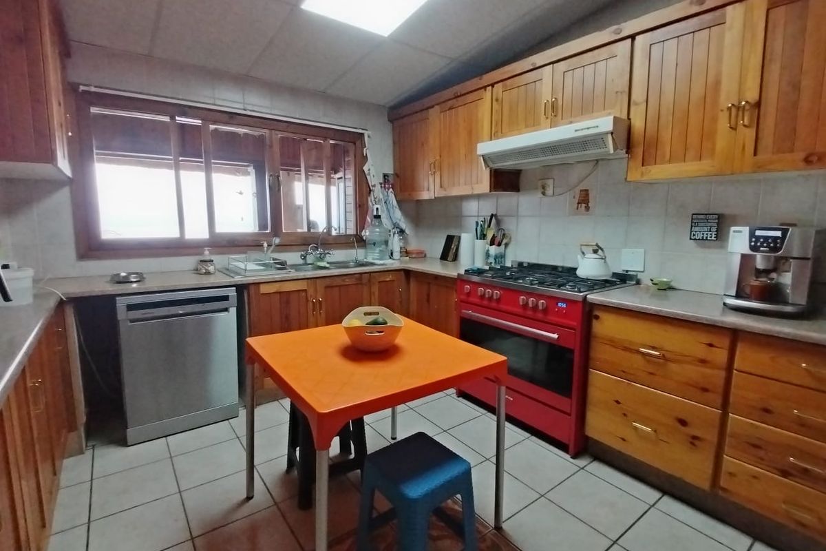 A functional kitchen featuring wooden cabinetry, a red gas stove with oven, extractor fan, and tiled flooring with a central dining area.