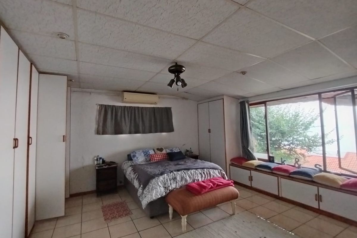 Spacious bedroom featuring built-in cupboards, tiled flooring, a split-system air conditioner, and a built-in window seat with storage.