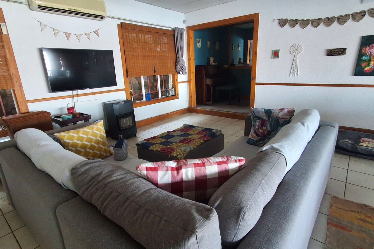 A living room featuring tiled flooring, timber trim, and a wall-mounted air conditioning unit, with an adjacent room visible through a wide doorway.