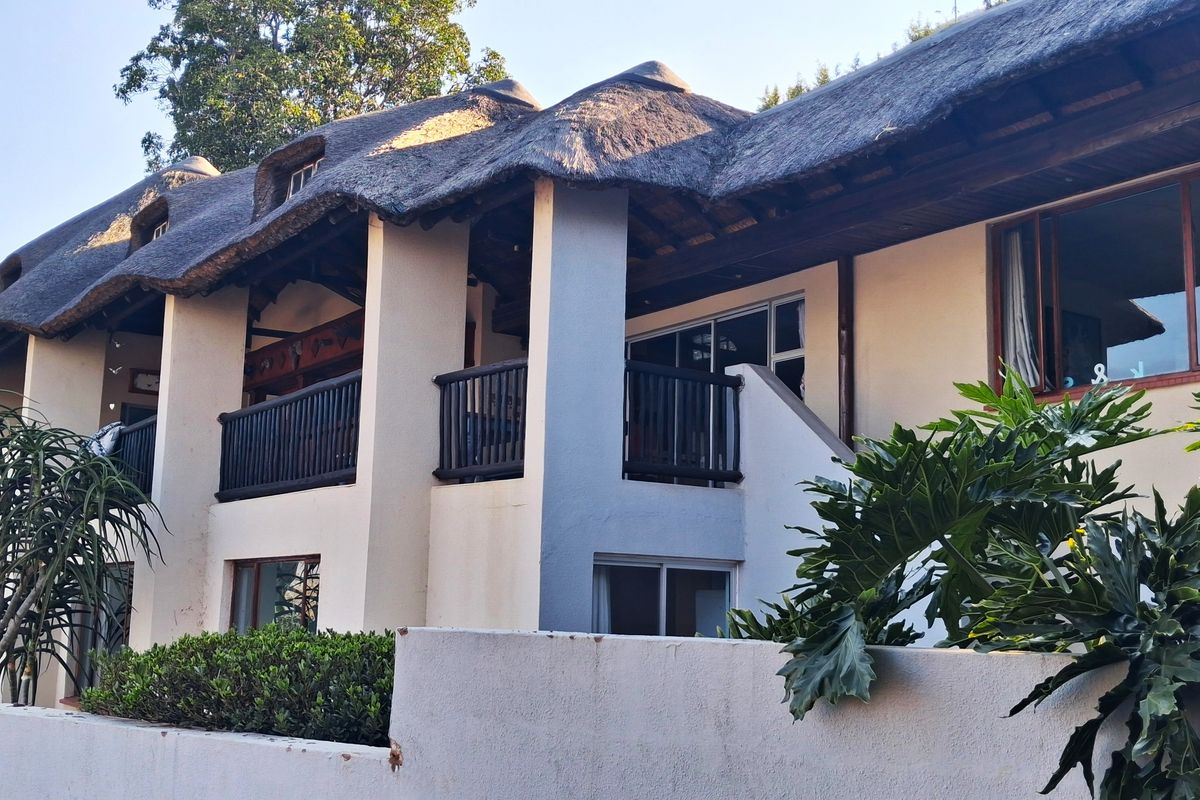 Rear elevation of a double-story residence featuring a traditional thatch roof, upper-level balcony with timber balustrades, and sliding door access.