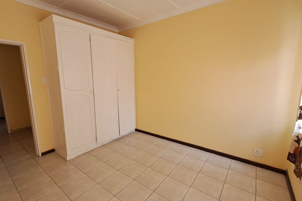 A clean, empty bedroom featuring neutral walls, tiled flooring, and a built-in wardrobe, offering a versatile space ready for personalization.
