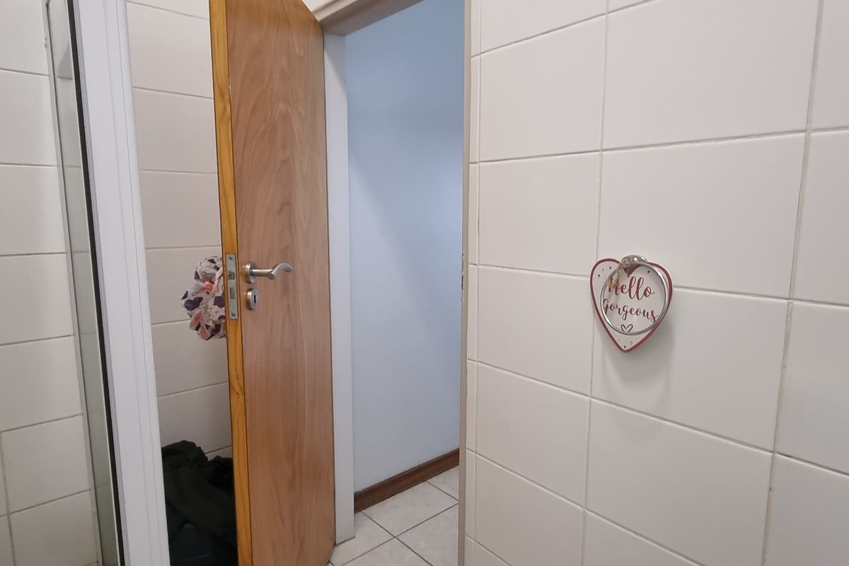 A functional bathroom space featuring neutral ceramic wall and floor tiles with a wooden door entrance.