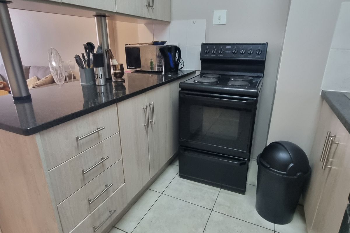 Compact kitchen featuring light wood-finish cabinetry, dark granite countertops, and a freestanding electric stove, seamlessly integrated with the adjacent living area.