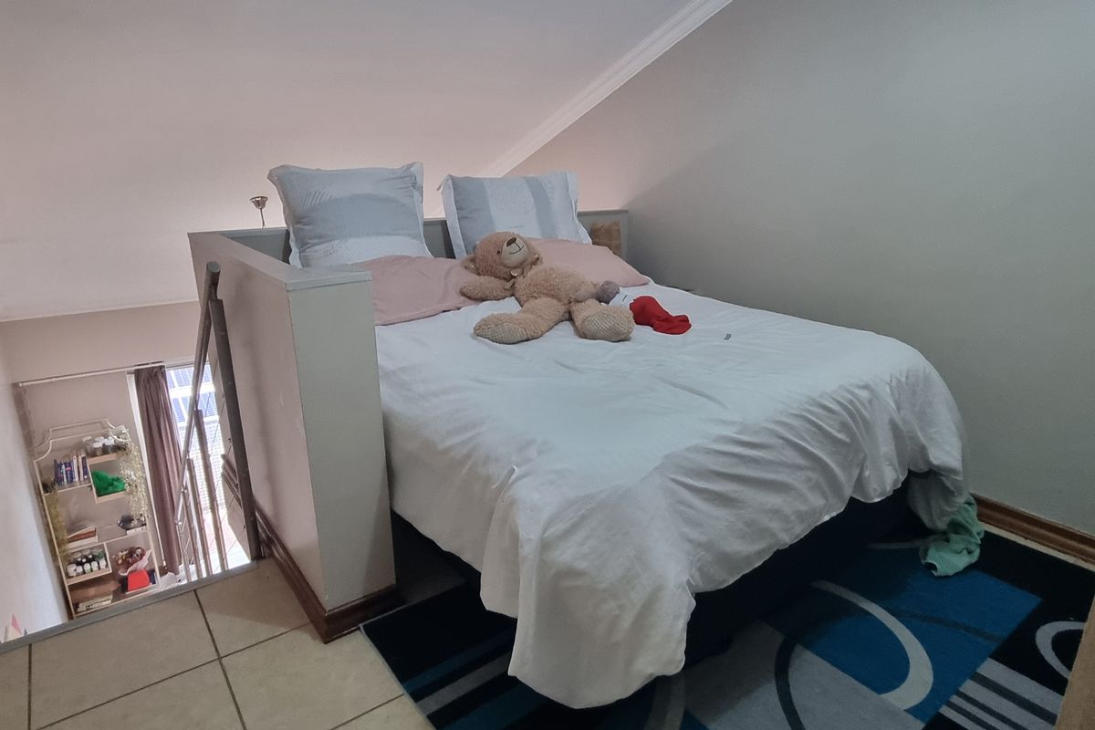 A mezzanine bedroom area featuring a raised sleeping platform accessible via a staircase, with neutral wall finishes and tiled flooring.