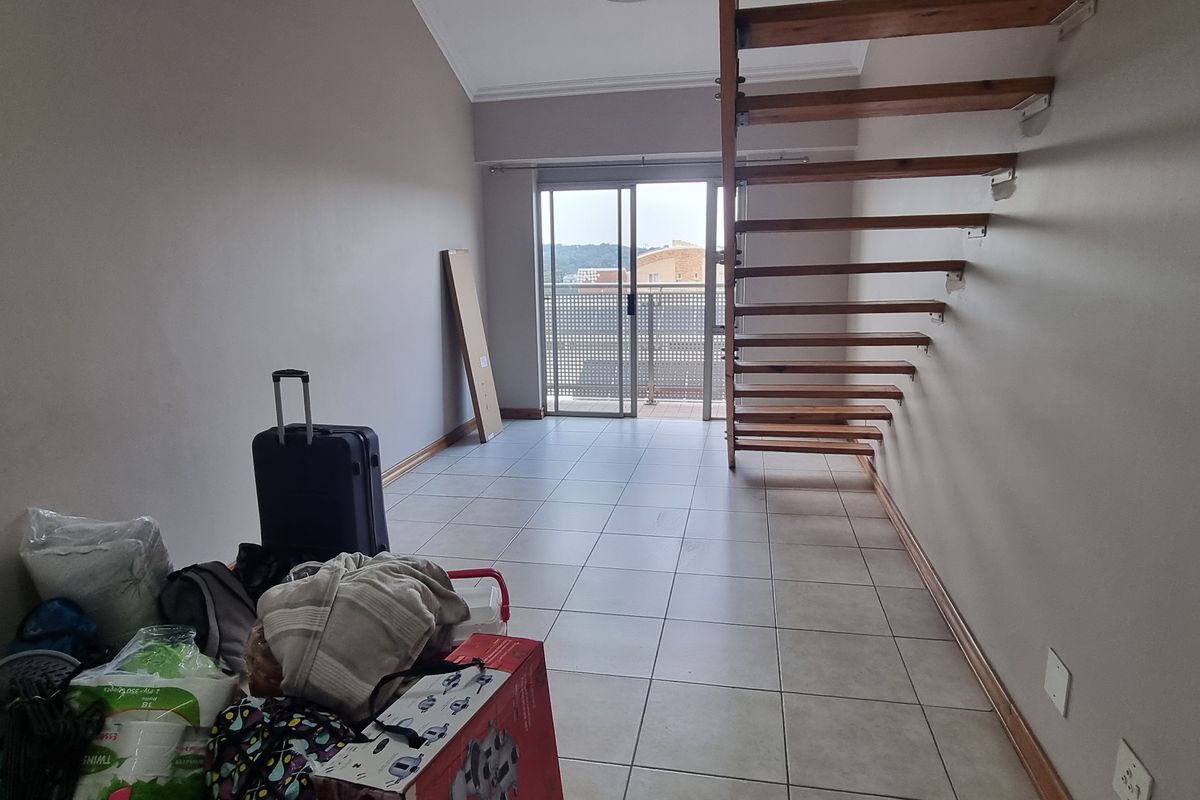 Open-plan living area featuring tiled flooring, a modern open staircase, and sliding glass doors leading to a balcony.