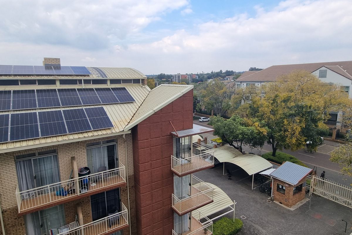 Aerial view of an apartment complex featuring a roof with installed solar panels, brick exterior, and associated parking facilities.