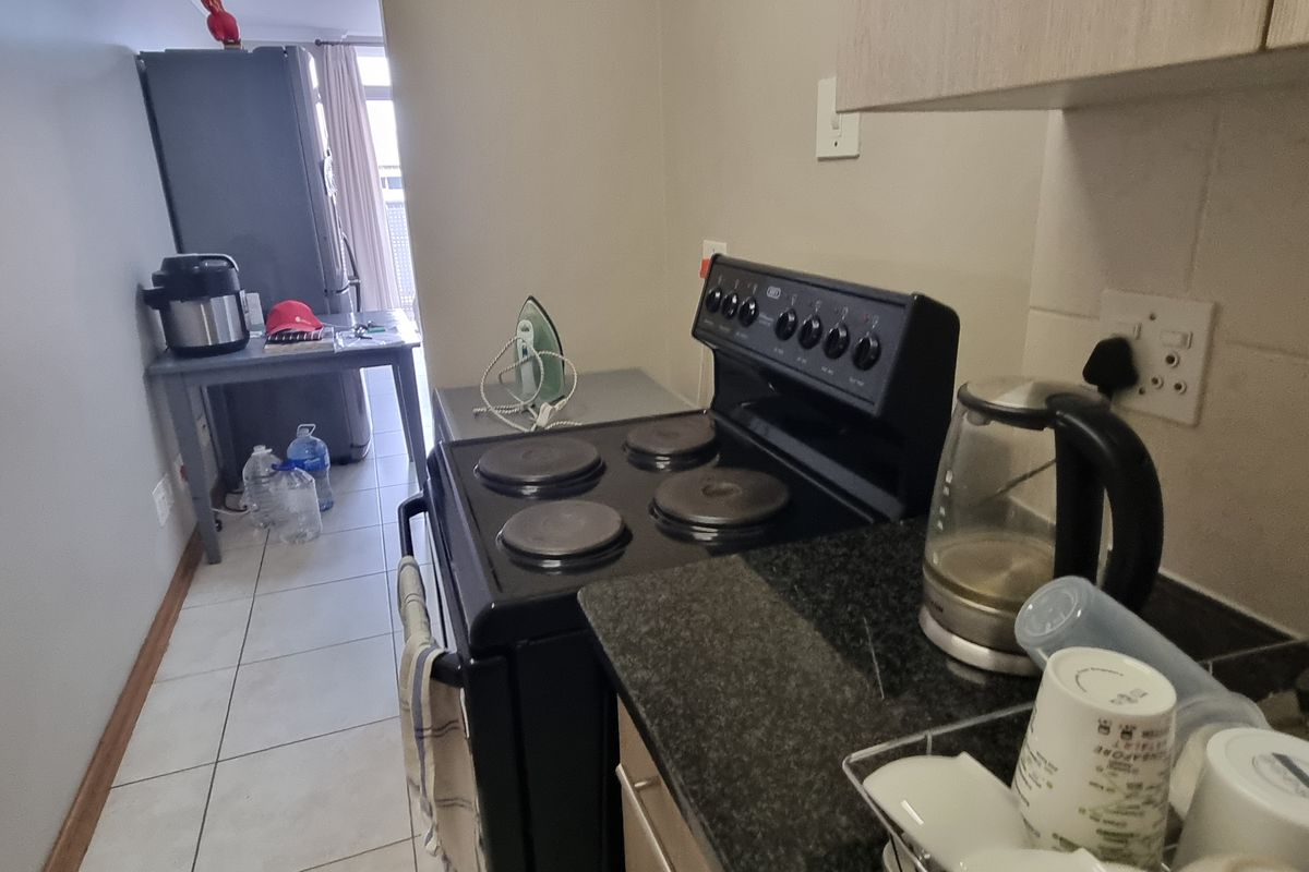A functional kitchen area featuring a black electric stove, granite countertops, and tiled flooring, leading towards an adjacent living space.