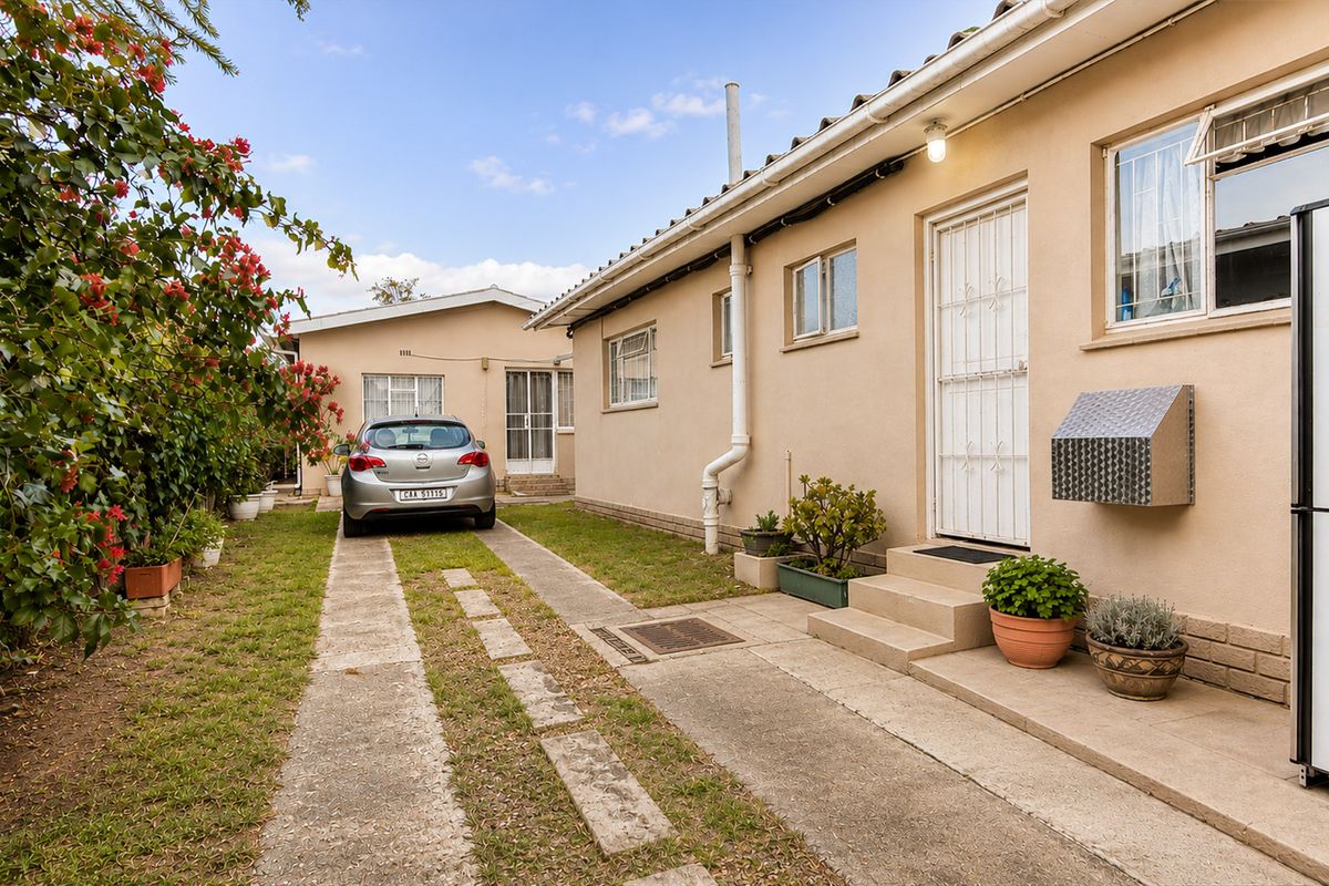 Exterior view of the property featuring a concrete driveway, side entrance with security gate, and established garden area.