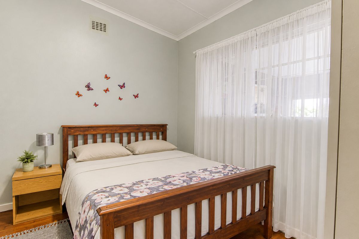 A well-maintained bedroom featuring timber flooring, neutral wall tones, and a built-in ventilation vent.