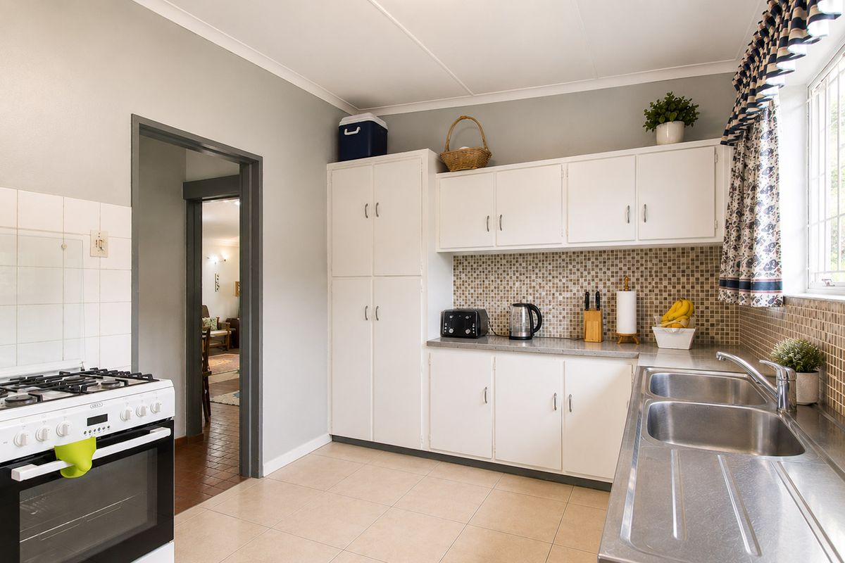A functional kitchen featuring white cabinetry, a mosaic tile backsplash, a stainless steel double sink, and a freestanding gas stove.