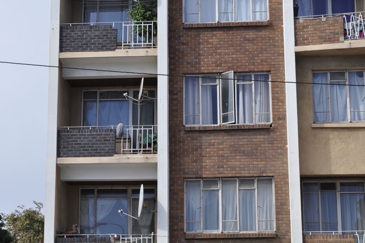 Exterior view of a multi-story apartment building featuring brick facade, private balconies with metal railings, and multiple window units.
