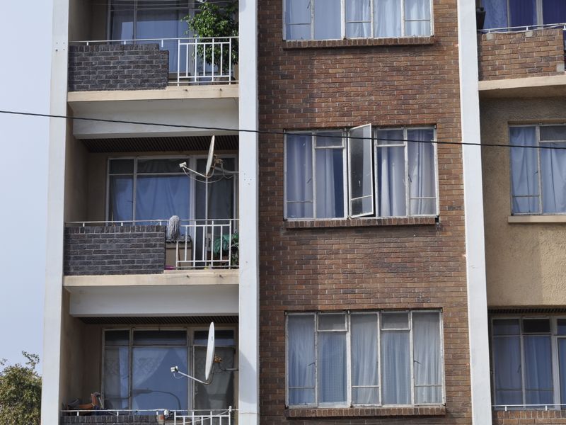 Exterior view of a multi-story apartment building featuring brick facade, private balconies with metal railings, and multiple window units.