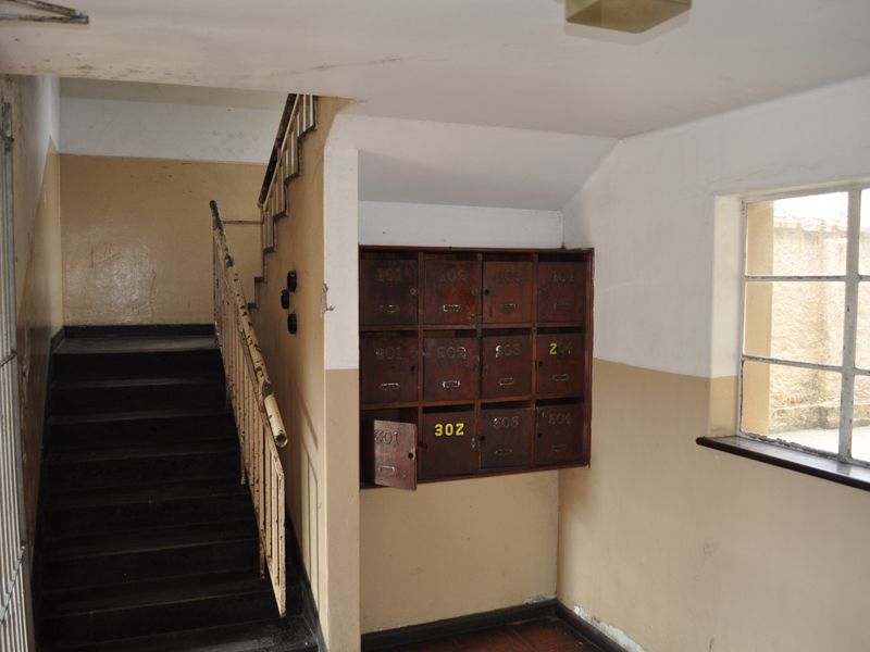 Communal apartment hallway featuring a staircase, metal handrail, and a bank of wall-mounted mailboxes.