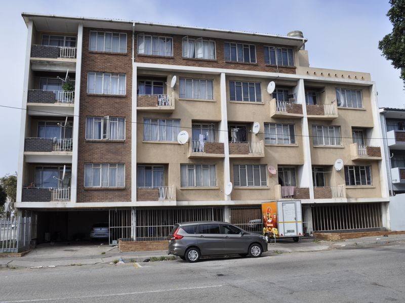Front elevation of a multi-story apartment building featuring brick and rendered facade, private balconies, and ground-level secure parking access.