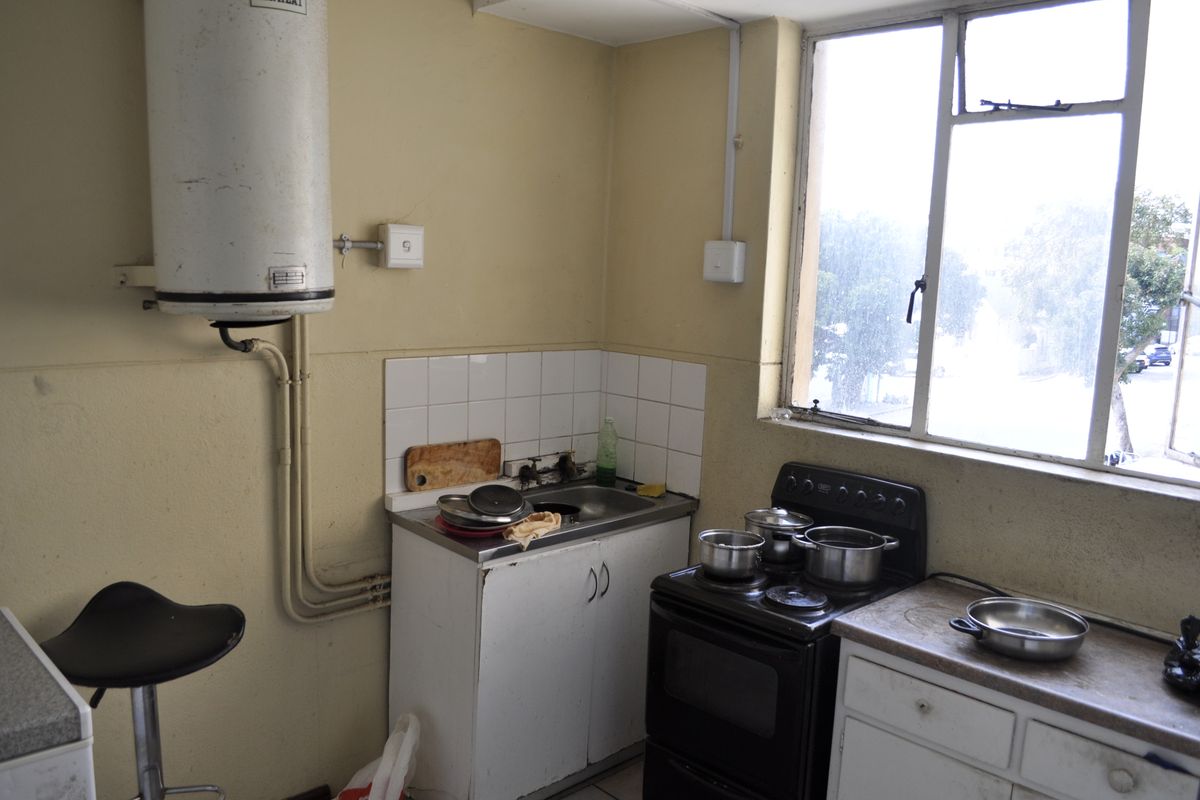 A compact kitchen featuring a stainless steel sink, freestanding electric stove, and wall-mounted water heater, requiring cosmetic updates to modernize the space.