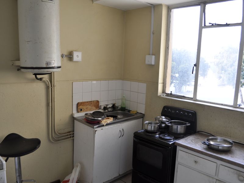 A compact kitchen featuring a stainless steel sink, freestanding electric stove, and wall-mounted water heater, requiring cosmetic updates to modernize the space.