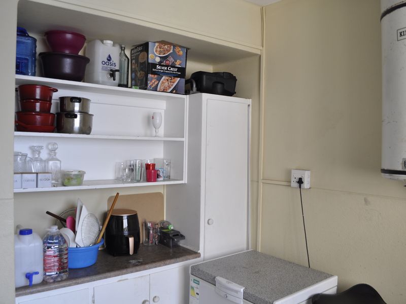 A functional scullery or utility area featuring built-in shelving, laminate countertops, cabinetry, and a wall-mounted electric water heater.
