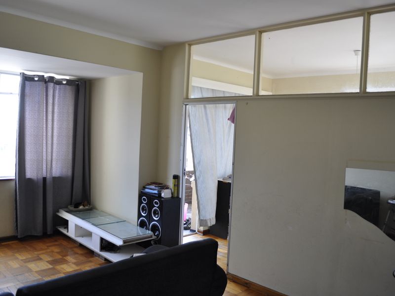 Living room featuring parquet flooring and a partition wall with transom windows, offering a functional layout with potential for cosmetic updates.