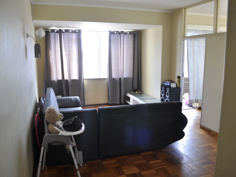 A living room featuring traditional parquet flooring, large windows for natural light, and a transom window above the doorway leading to an adjacent space.