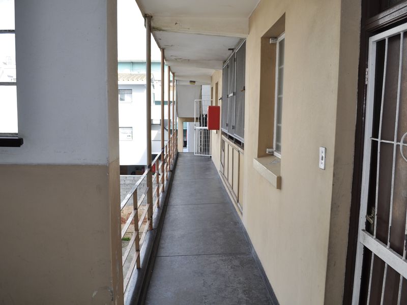 An exterior apartment building walkway featuring concrete flooring, metal security gates, and a metal balustrade overlooking the surrounding area.