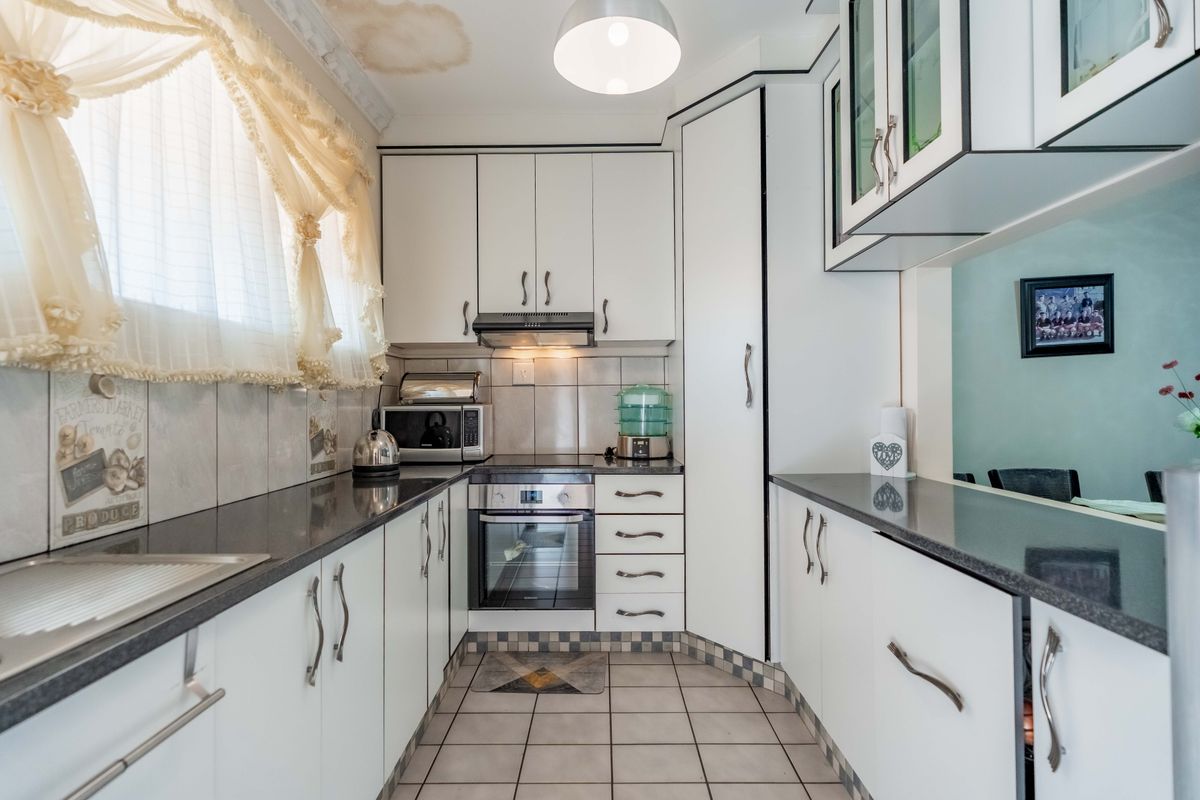 Compact kitchen featuring white cabinetry, dark granite countertops, and built-in appliances, with visible water damage on the ceiling requiring attention.