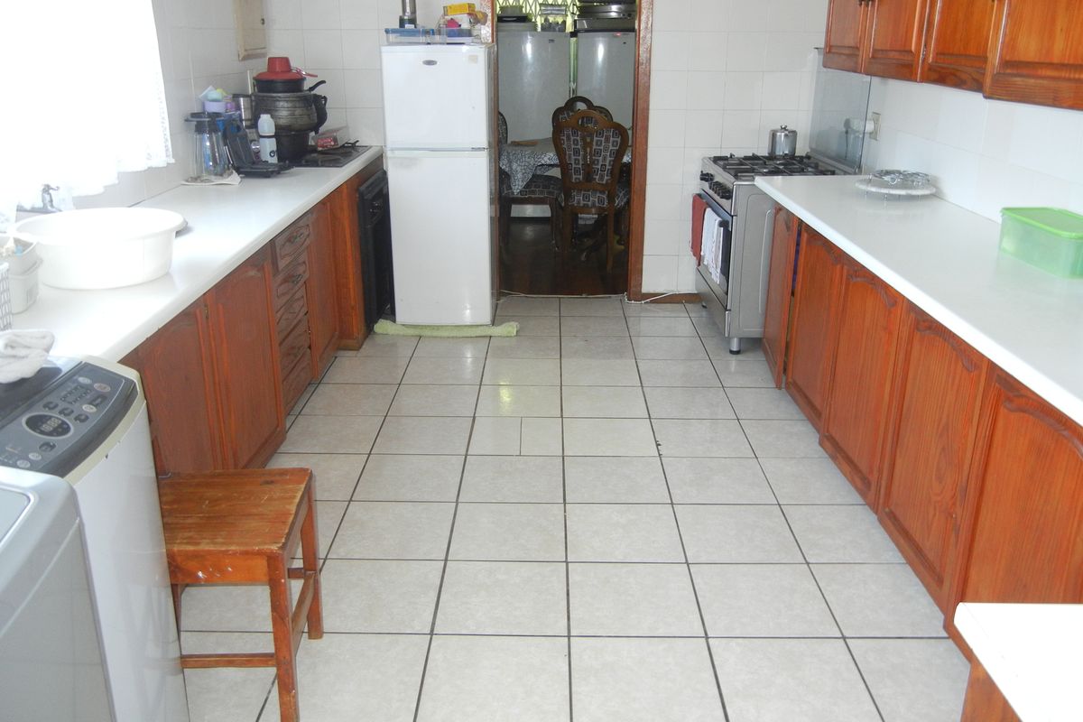 A dated kitchen featuring wooden cabinetry, tiled flooring, and a freestanding stove, offering a functional layout with potential for modern renovation.
