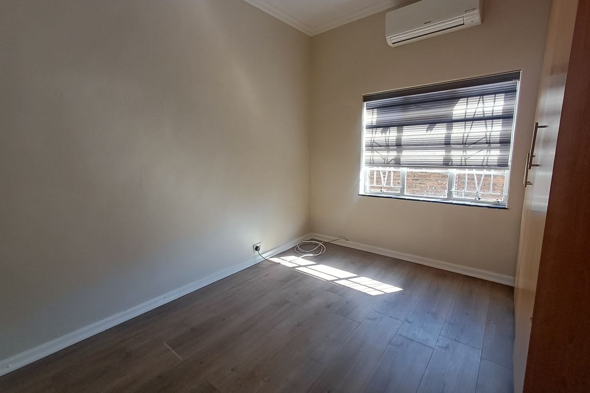 A clean, empty bedroom featuring laminate flooring, a built-in wardrobe, and a wall-mounted air conditioning unit.
