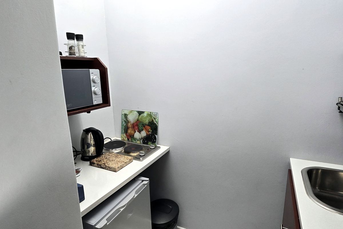A compact kitchenette featuring a built-in electric hob, stainless steel sink, and wall-mounted storage shelving for efficient food preparation.