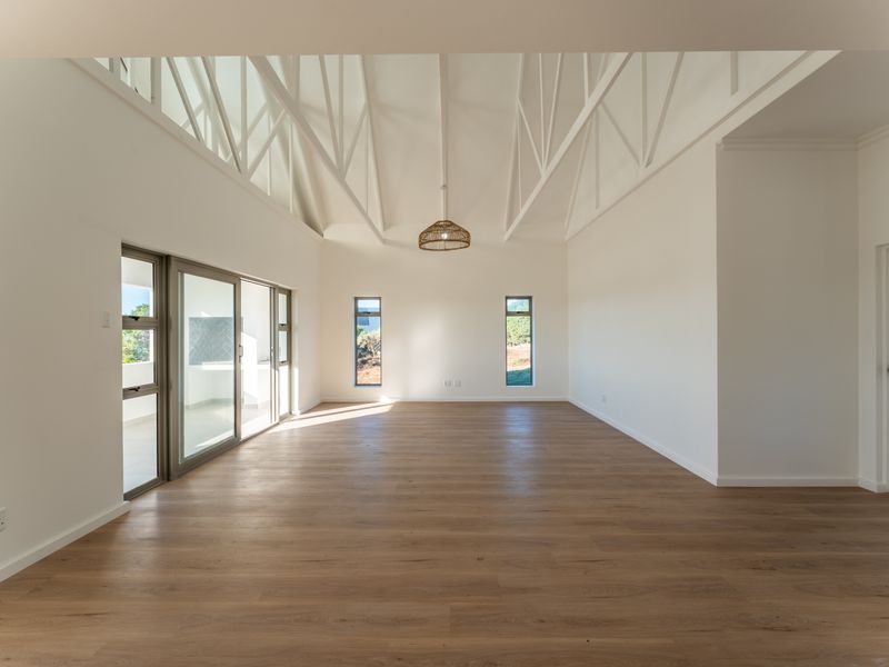 Spacious open-plan living area featuring high vaulted ceilings with exposed trusses, wood-look flooring, and large sliding glass doors leading to an outdoor space.