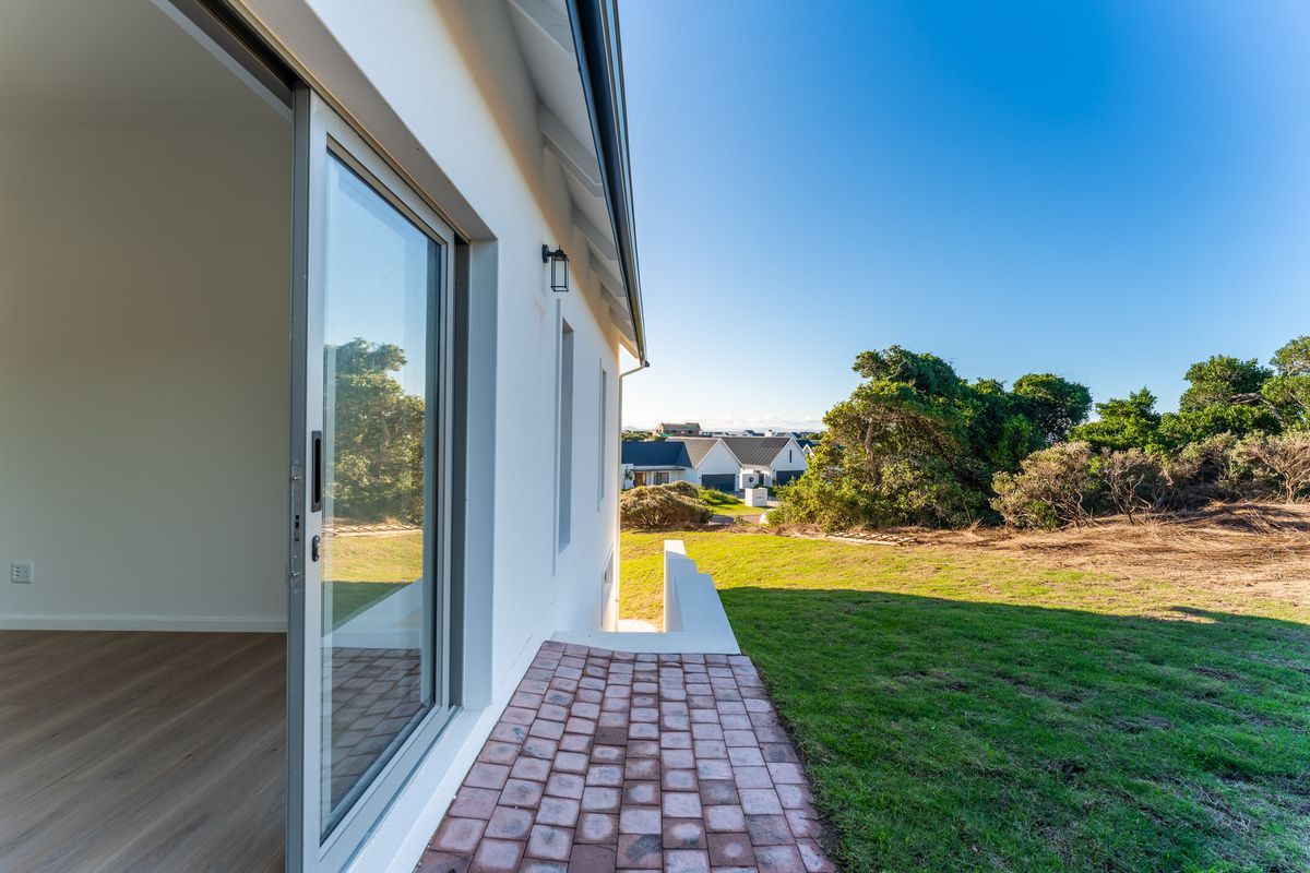 A view of the exterior rear of the property, featuring a paved walkway, sliding glass doors, and a well-maintained lawn area.