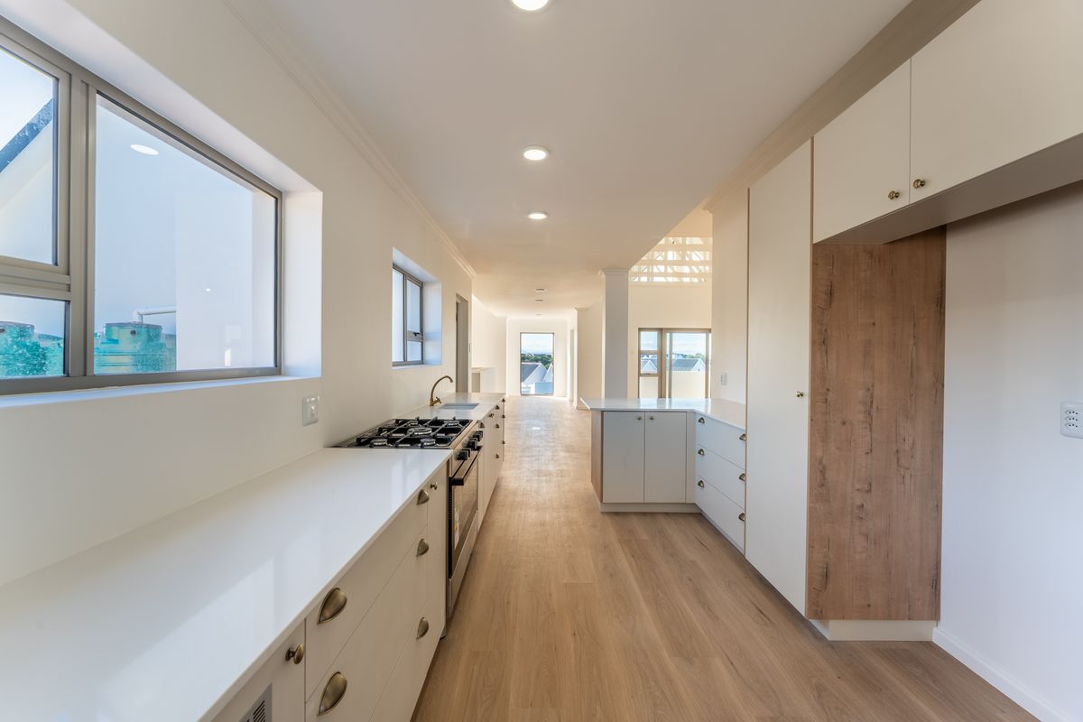 Modern galley-style kitchen featuring sleek white cabinetry, integrated gas hob, oven, and light wood-look flooring in a bright, open-plan layout.