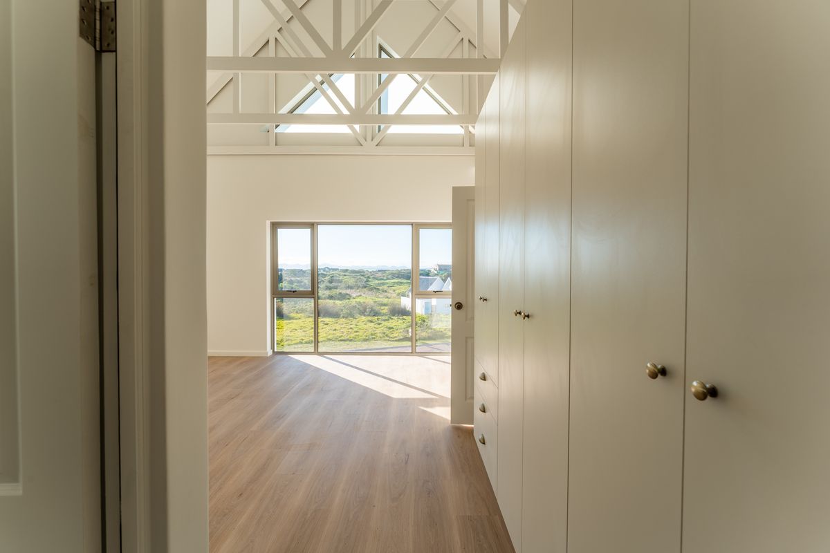 Bright bedroom featuring high vaulted ceilings with exposed trusses, built-in floor-to-ceiling cabinetry, and large windows offering scenic landscape views.