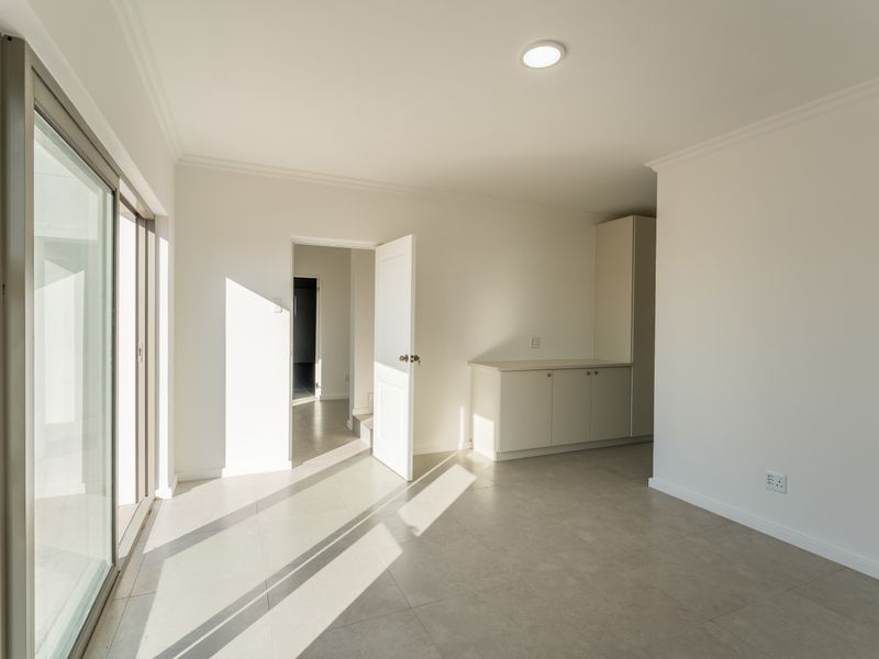 A bright, neutral living space featuring tiled flooring, built-in cabinetry, and large sliding glass doors providing access to the exterior.