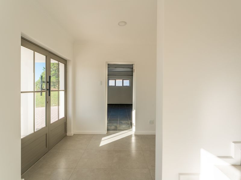 A bright and modern entrance hall featuring large glass-paned double doors, neutral floor tiles, and a clean, minimalist aesthetic leading into an adjacent room.