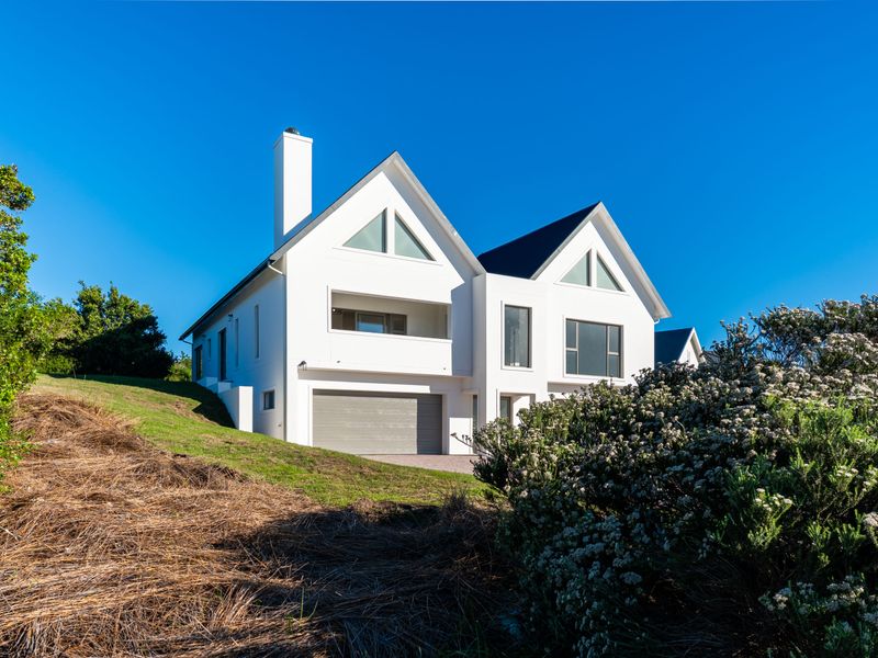 A modern, multi-level white residential home featuring a double garage, pitched rooflines, and triangular architectural windows set against a clear blue sky.