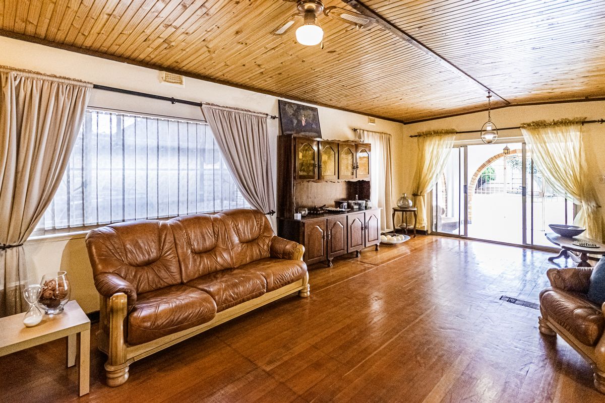 Spacious living room featuring warm timber flooring and a classic timber-paneled ceiling, with large windows and sliding doors providing ample natural light.