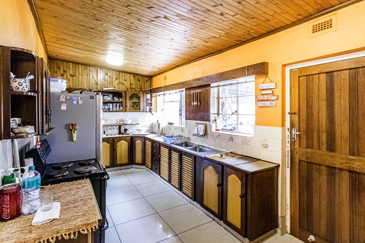 A functional kitchen featuring timber ceiling paneling, tiled flooring, built-in cabinetry, and a double sink with ample counter space.
