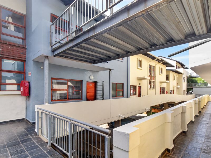 Exterior view of an apartment complex featuring a metal walkway, steel balustrades, and tiled access corridors.